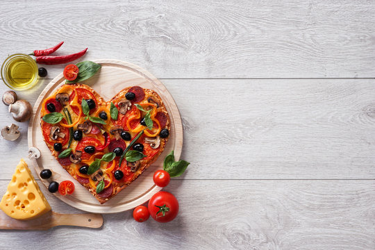 Pizza heart shape with ingredients and copy space on white wooden background. High resolution product.