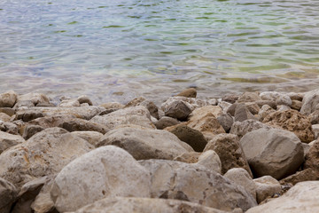 White yellow grey natural boulders with salt levee on blue water edge of Dead Sea with ripples