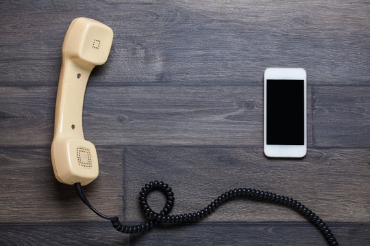 Old retro phone and new cell phone on wooden board, top view