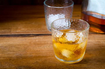 Bottle and glass of whiskey with ice on a wooden background