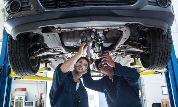 Mechanics examining silencer of a car using flashlight