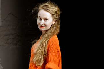 Young beautiful long-haired hipster girl on a sunny day outdoors. Lifestyle portrait of a woman dressed in colorful sweater with city in the background. Concept of freedom and happiness.