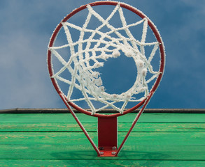 A basketball hoop with a net in the frost on blue sky background close up shot from below