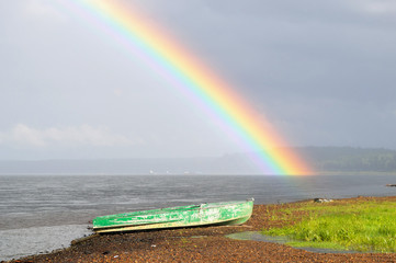 Green metal boat, standing on the starboard side on the background of a bright rainbow over a wide river