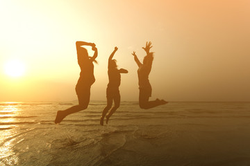 Fototapeta premium Silhouette of three young girls jumping with hands up on the be
