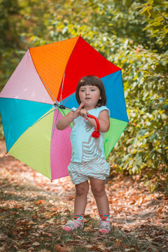 Little girl playing in summer park. Child holding umbrella walking in the forest on a sunny fall day. Children playing outdoors. 