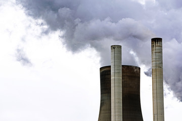 chimneys and a cooling tower of a power plant steaming gray clouds