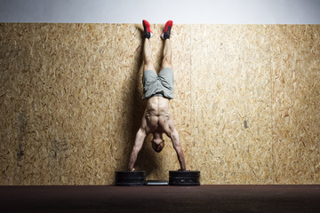 Bodybuilder doing handstand at the wall in the gym