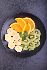 sliced fruit (strawberries, kiwi, orange, banana) on a black plate