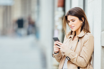 Beautiful young woman standing at the street and using her mobile phone