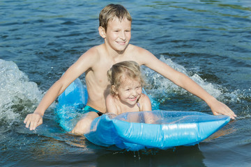 Siblings having fun during summer sea bathing with robin egg blue pool air mat outdoor