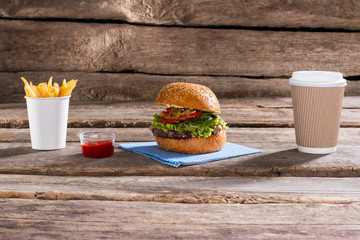 Burger and paper coffee cup. Hamburger with coffee on table. Lunch in fast food restaurant. Quick boost of energy. 
