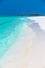 Tropical island with sandy beach, palm trees, overwater bungalows and tourquise clear water.