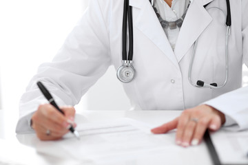 Close-up of a female doctor filling  out application form , sitting at the table in the hospital