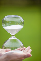 Hands hold an hourglass on green background. Concept for business deadline and leadership