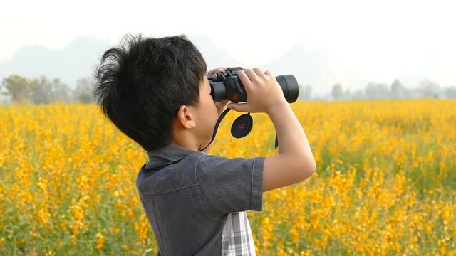 Asian boy looking through binoculars in flower field