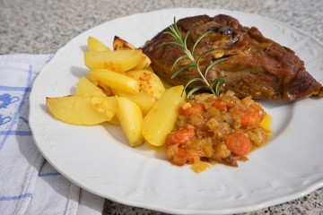 Slowly roasted spring lamb leg with rosemary and garlic served with sweet glazed onions, carrots, apples and baked potatoes on the simple rustic white plate. Fresh homemade dish for lunch or diner.