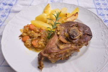 Slowly roasted spring lamb leg with rosemary and garlic served with sweet glazed onions, carrots, apples and baked potatoes on the simple rustic white plate. Fresh homemade dish for lunch or diner.