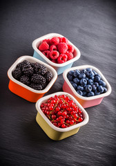 Berries assortment in four ceramic jars on dark background
