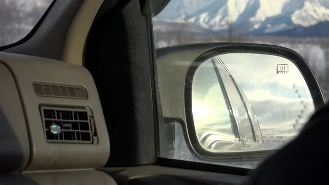 View of the right side mirror of the car in the mountains and snow-capped peaks of the northern slopes