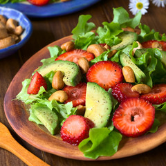 Strawberry, avocado, lettuce salad with cashew nuts on plate, photographed on dark wood with natural light (Selective Focus, Focus in the middle of the salad)