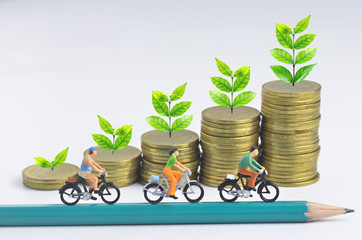 Fototapeta na wymiar Miniature people cycling on pencil and stack of coins background