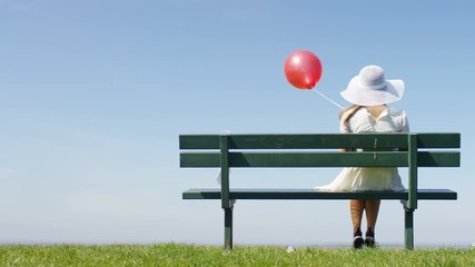 4K Female in a sun hat sitting on a bench, holding a red balloon - Powered by Adobe