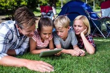 Fototapeta premium Family lying on grass and using digital tablet