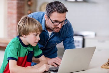 Father and son using laptop in kitchen