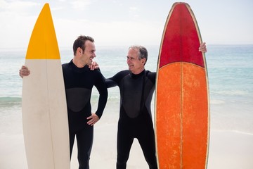 Father and son with surfboard standing on beach