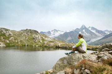 Fototapeta na wymiar woman sitting on rock and looking at mountain lake