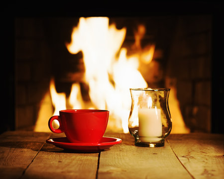 Red cup and candle on wooden table near fireplace.