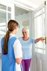 Obraz premium Smiling senior woman standing with nurse by door