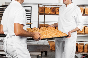 Midsection Of Baker's Carrying Bread Loaves In Tray