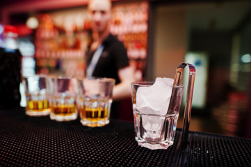 Glass with ice and tongs with three whiskey glasses background b
