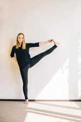 Blonde girl standing in asana near a white wall