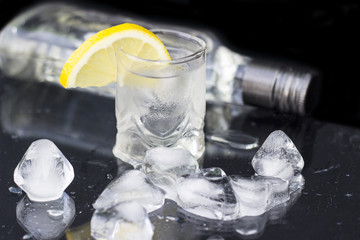 A glass of vodka with ice and lemon on a black background, close-up