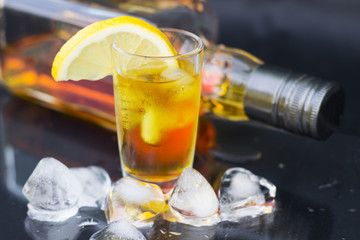 A glass of cognac with ice and lemon on a black background, close-up
