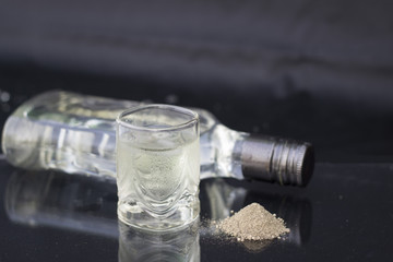 A glass of vodka on ice on black background, black ground pepper