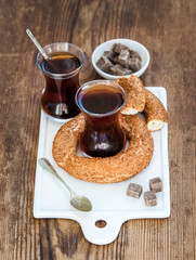 Turkish traditional black tea in a glass and turkish bagel simit on white ceramic serving board over wooden background