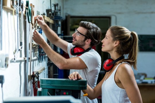 Male and female carpenter selecting a tools from hanging bar