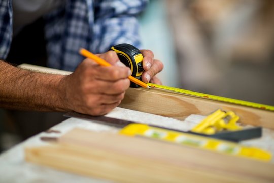 Carpenter marking on wooden plank with pencil