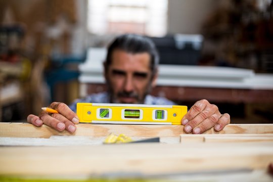 Carpenter measuring a length of wooden plank with spirit level