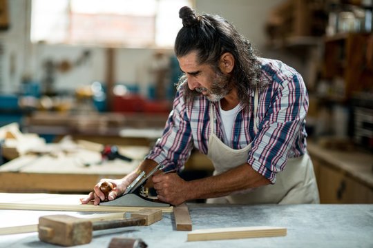 Male carpenter leveling a timber with jack plane