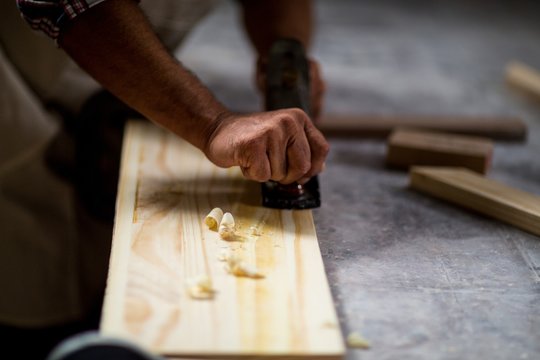 Male carpenter leveling a timber with jack plane