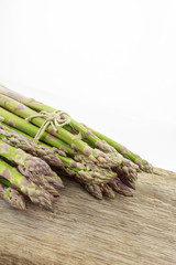 Two bunches of asparagus tied with raffia cord on wooden surface with copy-space, on white background.