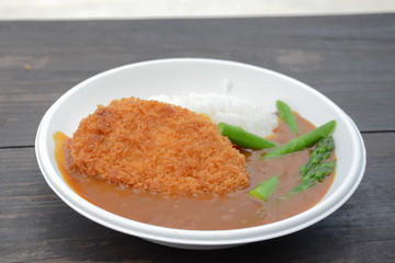 Curry rice with fried pork and asparagus on white plate on wood table