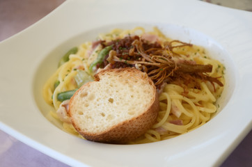 Spaghetti with white sauce, ham, roasted mushroom and bread on white plate