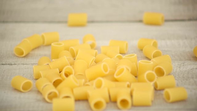 Hands pouring Mezze Maniche pasta onto wood 