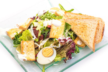 fresh vegetable arugula salad with cheese, eggs and bread slices on glass plate isolated on white background, product photography for restaurant or healthy lifestyle